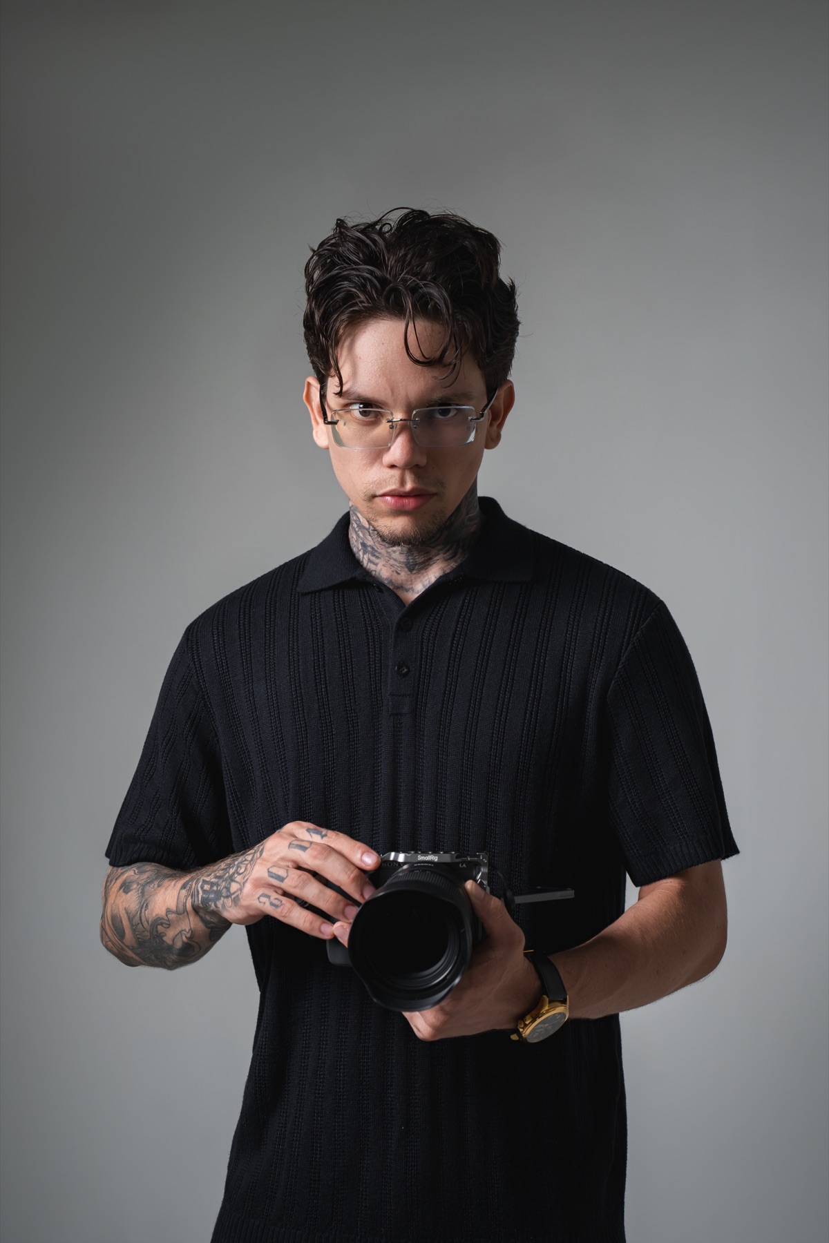 Edu Belmont, de camisa preta, segura uma câmera em um estúdio de fundo cinza.