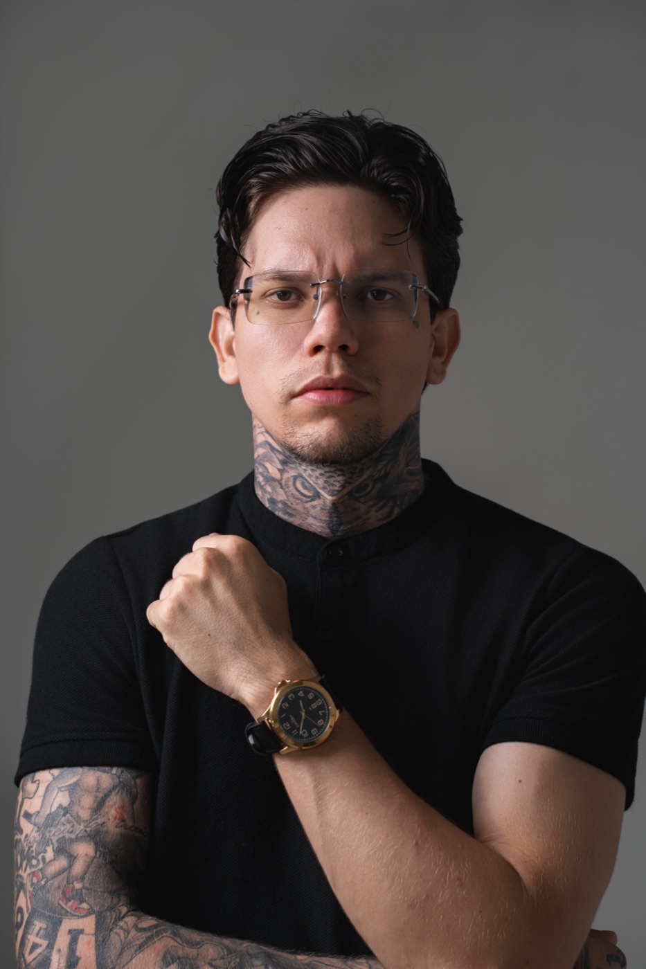 Retrato de Edu Belmont, de camiseta preta e relógio, em fundo cinza.